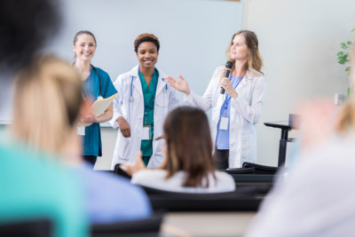 Three female doctors talking to a lecture hall full of peers
